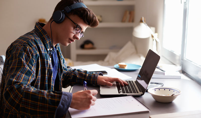 Photo of student with headphones working at a laptop computer
